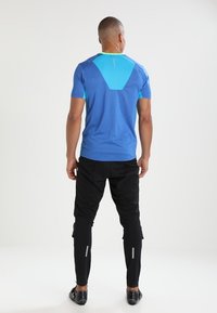 Camiseta deportiva azul de mangas cortas, con acentos en turquesa en contraste y un diseño texturizado en la parte posterior; combinada con pantalones ajustados negros que cuentan con tiras reflectantes.