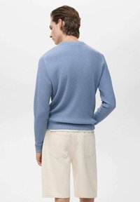 Suéter azul de canalé con mangas largas, escote redondo y un corte relajado, combinado con pantalones cortos de color claro. Tejido simple y texturizado.