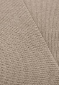 Beige gebreide stof met een gladde textuur, voorzien van fijne ribbreipatronen en een zachte, flexibele samenstelling.