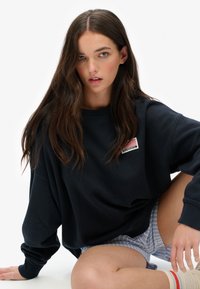 Navy oversized sweatshirt made of cotton with a round neckline and long sleeves, featuring a small American flag emblem on the chest.