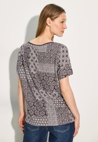 Kortærmet top med et mørkelilla og hvidt patchworkmønster, der har blomster- og geometriske designs, rund halsudskæring og afslappet pasform.