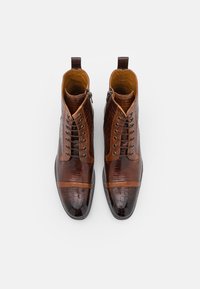 Pár lesklých hnědých kožených kotních bot na šněrování s krokodýlí texturou a bočními zipy na bílém pozadí.