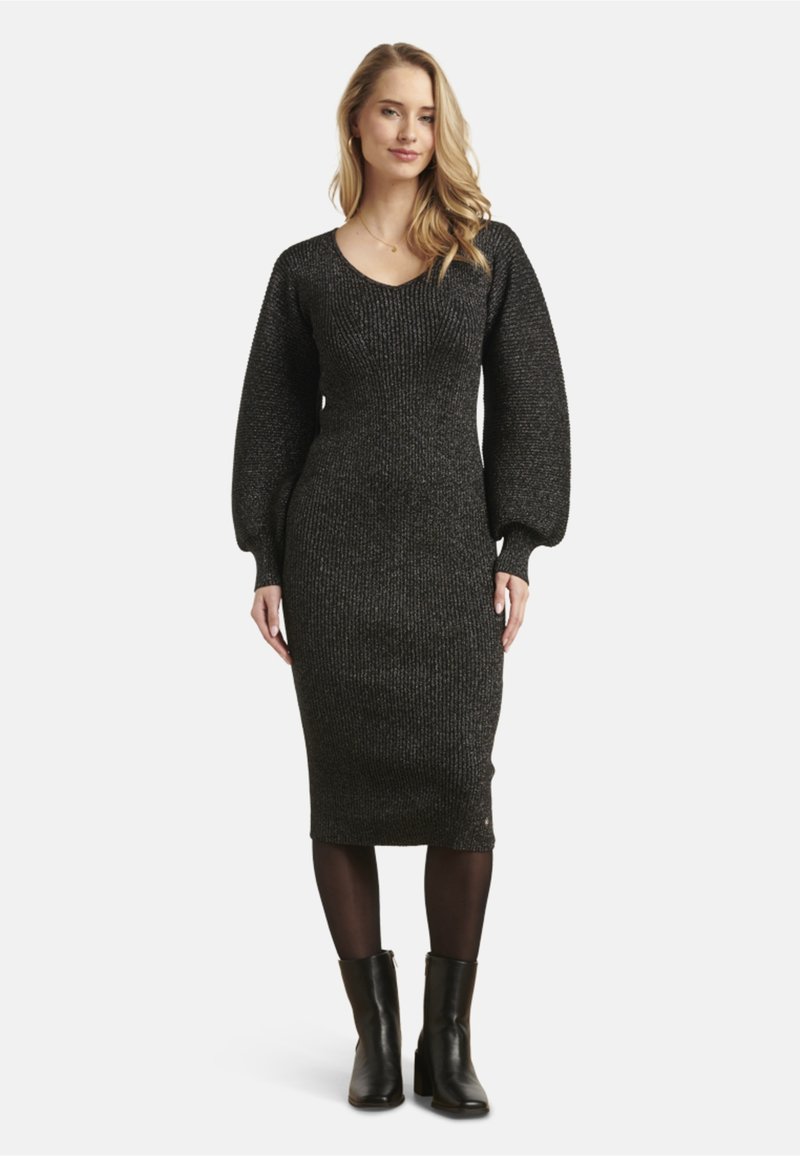 Black ribbed knit dress with a fitted silhouette, deep V-neck, and puffed long sleeves. Worn with black heeled ankle boots.