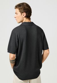 Kortärmad polotröja i mörkgrått, texturerat tyg, med en vikbar krage, rak nederkant och subtila sömdetaljer.