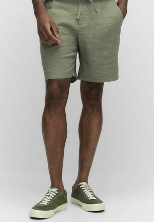Khaki green shorts made of lightweight fabric, featuring a drawstring waistband and side pockets. Paired with green sneakers and white laces.