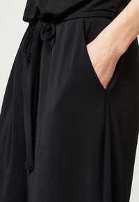 Black pants with a drawstring waistband and soft fabric, featuring side pockets and a smooth texture.