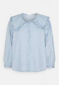 Chemise en denim bleu clair avec un grand col à volants, fermeture à boutons sur le devant, et manches longues avec poignets élastiques. Texture lisse avec des boutons brillants en accent.