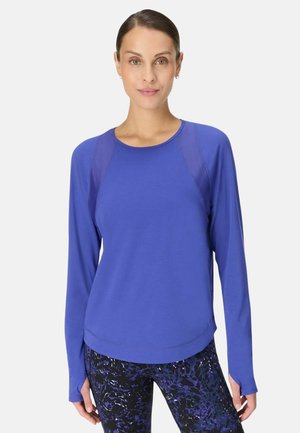 Blaues Langarmshirt mit rundem Ausschnitt und Raglanärmeln. Der Stoff wirkt glatt mit leichtem Glanz, kombiniert mit gemusterten Leggings.