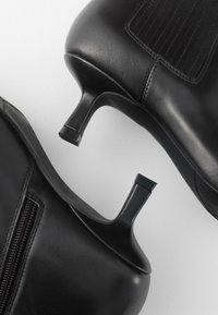 Paire de bottines en cuir noir avec talons courts effilés sur fond blanc.