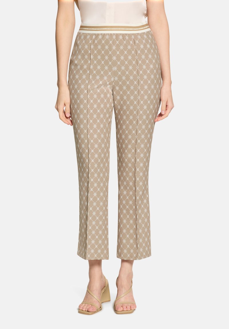 Pantalon beige court avec motif géométrique blanc, taille haute et jambes droites, porté avec des sandales compensées beiges à lanières.