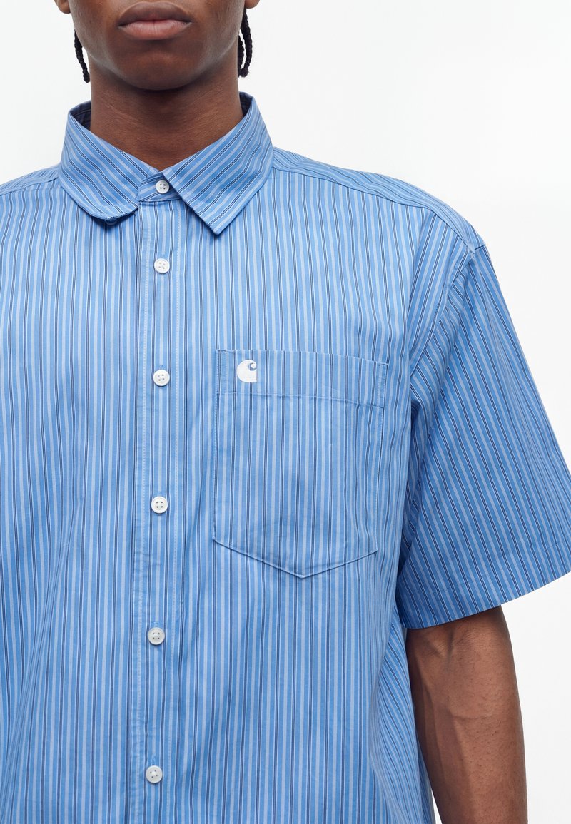 Male wearing a short-sleeve blue striped button-up shirt with a front chest pocket on a white background.
