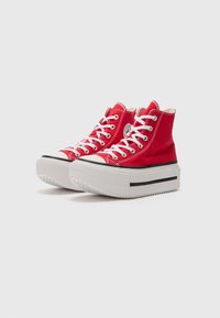 Röda högre sneakers i canvas med vita snören, en gummikappa på tån och en tjock vit plattformssula med ett svart rand.
