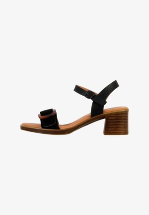 Sandale noire avec une large sangle et une boucle carrée. Présente un talon en bois brun avec des rainures horizontalement. Tige et semelle en cuir.