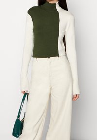 Sweter z golfem wykonany na drutach z wzorem w kolorowe bloki; oliwkowa zieleń i kolor kremowy, dopasowany fason, struktura prążkowana, długie rękawy. Styl casualowy.