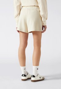Lichtbeige korte broek met een elastische tailleband, met een gladde textuur en een relaxte pasvorm. Gemaakt in combinatie met witte sokken en witte sneakers.