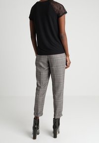 Black top with lace sleeves, gray checkered slim-fit trousers, and black heeled ankle boots. The overall look features a classic pattern.