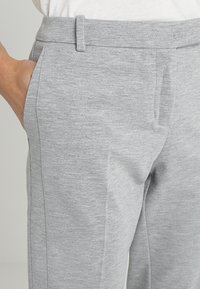 Pantaloni grigi chiari realizzati in un morbido tessuto testurizzato; presentano tasche anteriori e una vestibilità su misura con un discreto dettaglio a cucitura verticale.