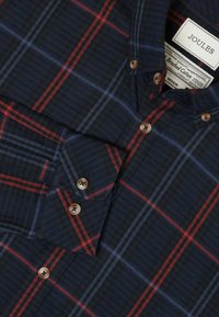 Granatowa flanelowa koszula z czerwono-niebieskim wzorem w kratę, z kołnierzykiem zapinanym na guziki oraz brązowymi guzikami z przodu i na mankietach.