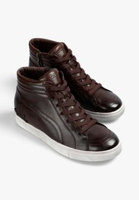 Zapatillas altas de cuero marrón con punta redonda, superficie texturizada y suela de goma blanca. Presentan un logo de calavera en el lateral y costuras decorativas.