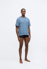 Kék texturált rövid ujjú póló környakkal, fekete rövidnadrággal párosítva. Minimalista kialakítás, légáteresztő anyag, kényelmes szabás.