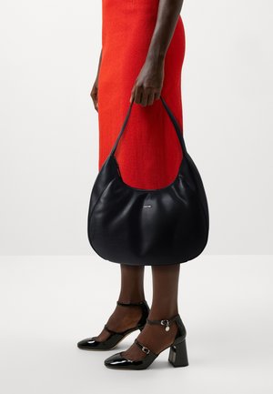 Sac hobo en cuir noir avec une texture lisse et une forme courbée. Il présente un logo à l'avant et une sangle d'épaule unique.