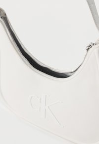 Λευκή δερμάτινη τσάντα ώμου με ασημί φερμουάρ και ανάγλυφο λογότυπο "cK" στο μπροστινό μέρος.