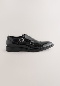 Chaussure habillée à double boucle monk en cuir noir poli avec bout fleuri et talon bas empilé, présentée sur un fond neutre.