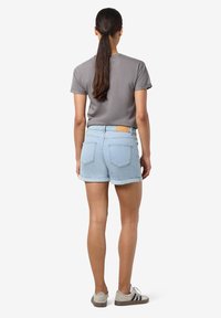 Pantalones cortos de mezclilla azul claro con un dobladillo enrollado, combinados con una camisa de manga corta gris. Presenta una etiqueta de cuero marrón en la cinturilla.