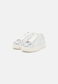 Weiße Sneakers mit einer glänzenden silbernen Zehenkappe, strukturiertem Synthetik-Obermaterial, flachen Schnürsenkeln und einer dicken weißen Sohle. "GUESS"-Logo an der Zunge und an der Seite.