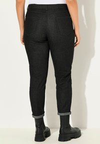 Pantaloni in denim nero con cintura elastica, risvolti e due tasche posteriori. Indossati con stivali chunky neri alla caviglia.