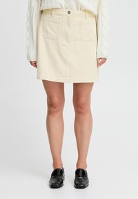 Jupe en velours côtelé beige clair avec taille ajustée, deux poches avant et coupe droite. Accompagnée de mocassins en cuir verni noirs.