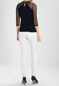 Granatowa bluzka z przezroczystymi koronkowymi rękawami i detalem w kształcie łezki z tyłu. Połączona z białymi wąskimi spodniami i czarnymi szpilkami.