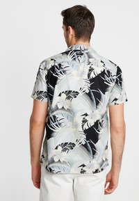 Camisa de manga corta con un patrón floral en negro y azul claro, fabricada en tela suave, con un cuello clásico y un corte relajado.