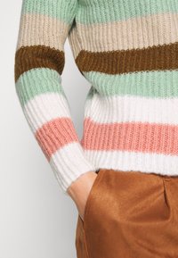 Maglione a righe nei colori menta, beige, marrone, rosa e bianco. Texture a coste e polsini aderenti. Abbinato a pantaloni in satin marroni.