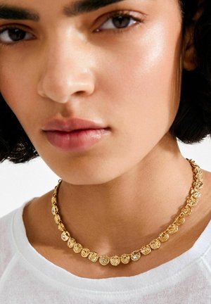 Auksinė vėrinys su apskritais ir širdies formos pakabukais. Kiekvienas pakabukas turi unikalią tekstūrą ir raštą, pritvirtintą prie subtilaus grandinėlės.