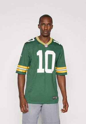 Zöld NFL mez, fehér 10-es számmal, sárga és fehér csíkokkal az ujján, valamint hálós textúrával. Szürke rövidnadrág felett viselve.