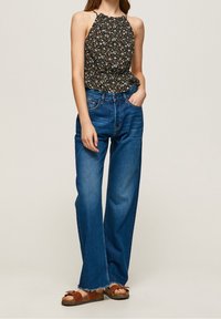 Czarny top halter w kwiaty z marszczonym pasem, zestawiony z niebieskimi dżinsami o szerokich nogawkach z postrzępionym dołem i brązowymi sandałami.