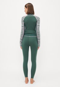 Long-sleeve green base layer top with patterned sleeves, paired with matching tight-fitting green leggings. Features contrasting stitching.