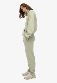 Lys grøn træningsdragt lavet af blød stof, med høj krave, oversized sweatshirt og tapered bukser med sidelommer. Båret med beige sneakers.