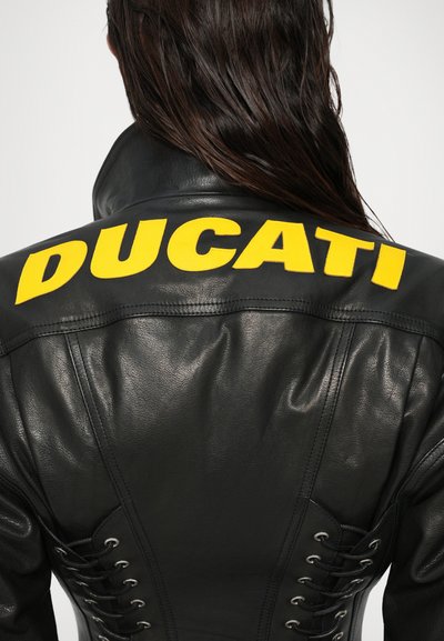 Sort læderjakke med et stort gult "DUCATI" logo på den øverste ryg. Siderne har snøredetaljer med metaløjer.