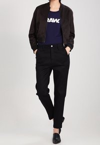 Černá bomber bunda s žebrovaným límcem, námořnická košile s potiskem "RAW!", sdružené černé kalhoty a černé slip-on boty.