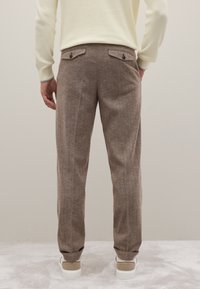 Bruine houndstooth broek met een op maat gemaakte pasvorm, voorzien van twee achterzakken en opgerolde cuffs, gecombineerd met witte en beige sneakers.