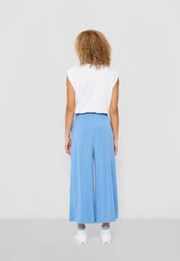 Light blue wide-leg pants made of soft fabric, featuring an elastic waistband. Paired with a white sleeveless top and white sneakers.