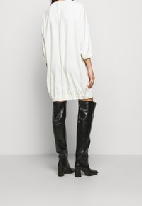 Vit klänning med trekvartsärmar, tillsammans med svarta knähöga klackstövlar med slät lädertextur och kvadratisk tå.