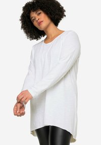 Witte tuniek met lange mouwen in een lichtgewicht, zachte stof met een ronde zoom en zijsplitten, gecombineerd met zwarte leggings.