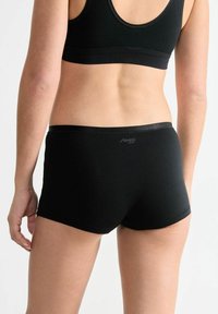 Black cotton hipster shorts with a smooth texture, elastic waistband, and a small logo on the back. Designed for comfortable fit.