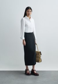 Biała koszula z długim rękawem, dopasowana czarna spódnica, brązowa torebka na pasku oraz bordowe platformy z wycięciami, stojące na jasnym tle.