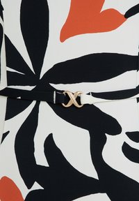 Tessuto con motivo floreale in nero, bianco e arancione, con una cintura nera dotata di una fibbia in metallo dorato a forma intrecciata in vita.