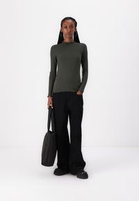 Ribbed, long-sleeve, olive green top with a scalloped neckline, paired with black wide-leg pants and a black, soft-textured tote bag.