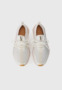 Par med hvite Sorel mesh-sneakers med snøring og brune innersåler, sett ovenfra mot en hvit bakgrunn.